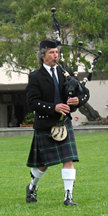 Image of bagpiper wearing a kilt and marching while playing bagpipes